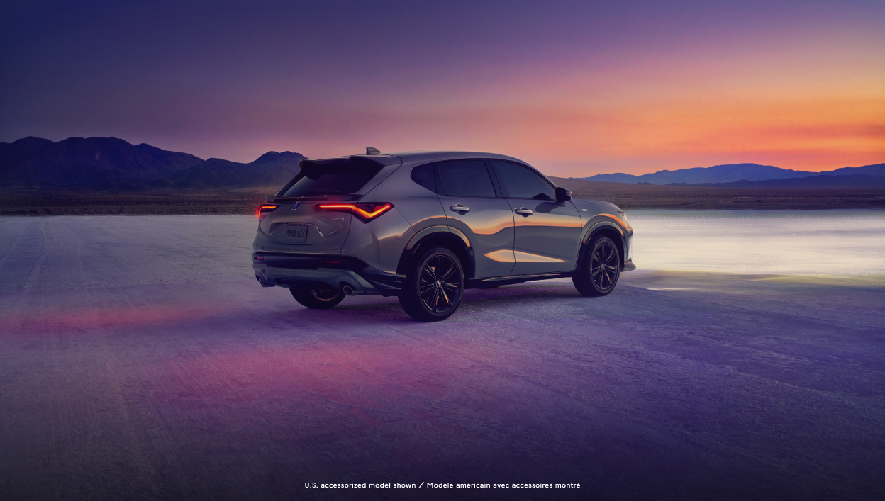 A 2025 Acura ADX is parked on a flat concrete lot with purple hues and a beautiful mountainous landscape in the background.