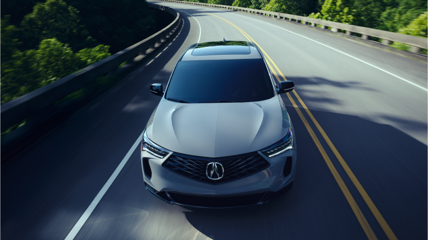 3/4 bird’s eye front view of grey RDX driving on highway on a sunny day.
