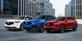 3/4 front view of a red RDX, blue MDX, and white ADX parked in a row with tall buildings in the background. 