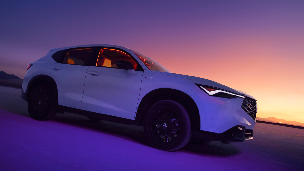 Side view of a white Acura ADX with a sunset in the distance. 