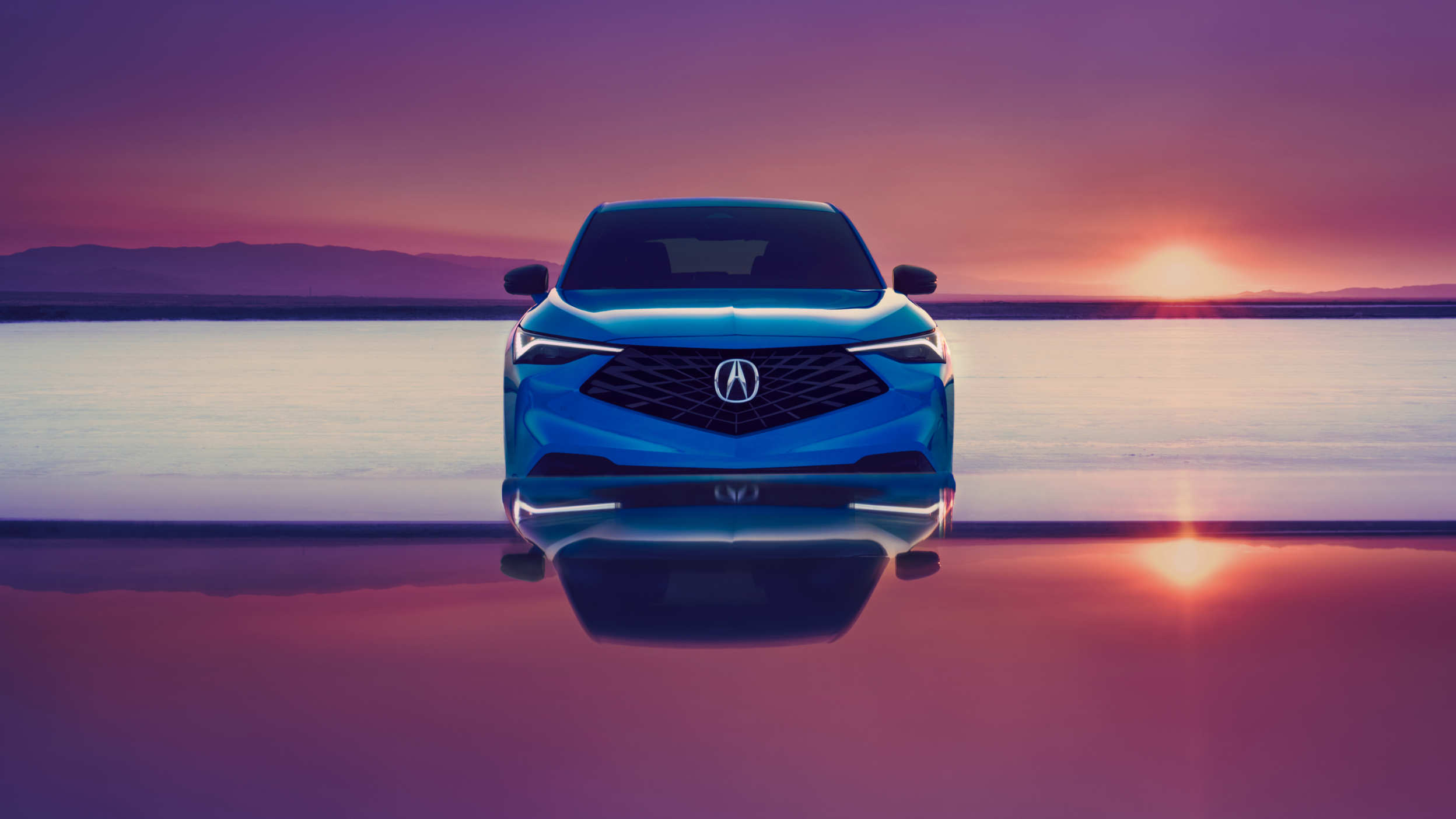 Front view of a blue Acura ADX with a sunset in the background.