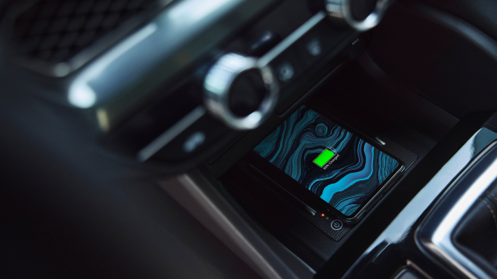 Closeup of smartphone charging on wireless charging pad in centre console.