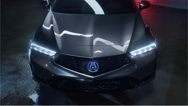 3/4 bird’s eye view of the hood and windshield of a grey Integra. Florescent lighting reflects off the hood while red light is reflected off the walls behind it.