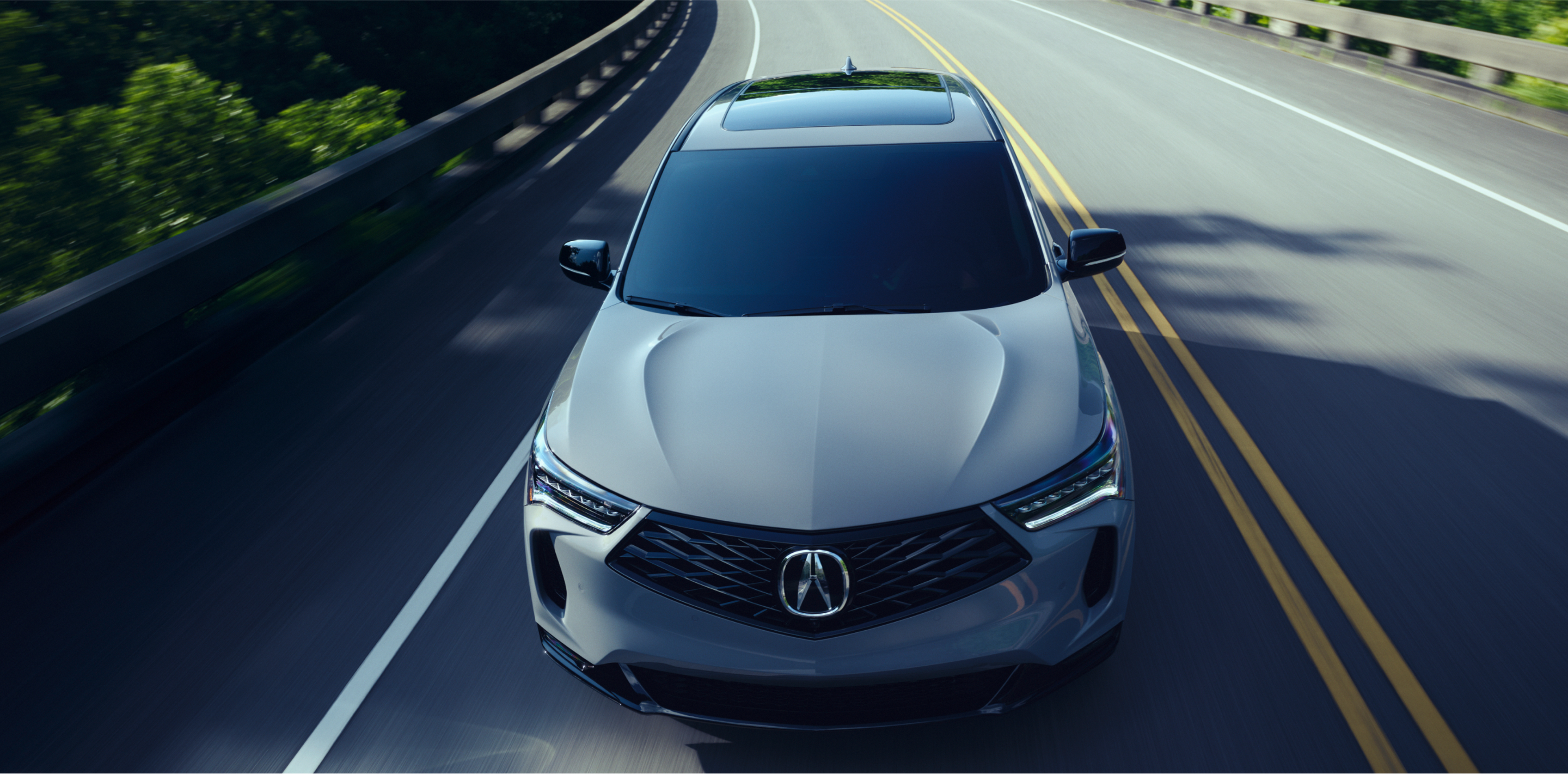 3/4 bird’s eye front view of grey RDX driving on highway on a sunny day.