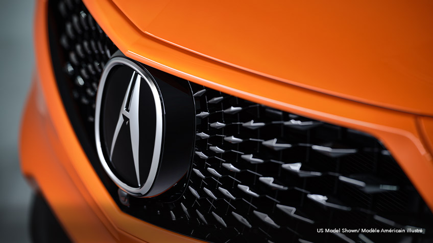 Close-up, angled view of the front grille on an orange Acura MDX. Gros plan en angle de la calandre d’un Acura MDX orange.